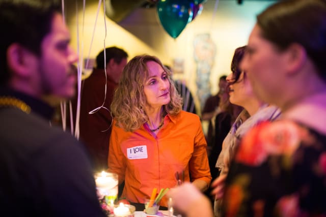 Woman in orange shirt engaging with guests at Love Bomb 2017 event, surrounded by balloons and festive decorations, highlighting community support for My Voice Music.